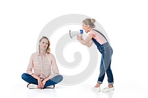 Little girl holding megaphone and screaming at pensive mother sitting