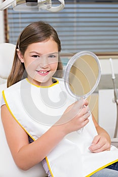 Little girl holding mirror in dentists chair