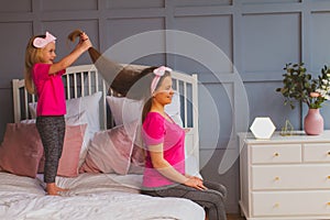 Little girl holding mothers long hair, standing on bed