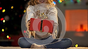 Little girl holding out Xmas present to camera, charity on Christmas benevolence