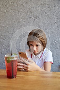 little girl holding phone, taking photo of red icy cocktail on table of cafe