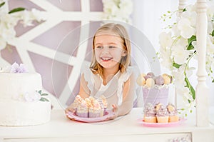 Little girl holding a pink plate with sweet cakes in the candy bar