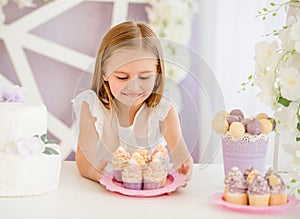 Little girl holding a pink plate with sweet cakes in the candy bar