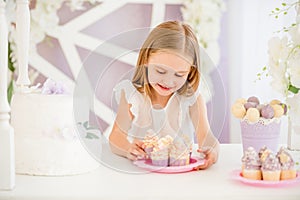 Little girl holding a pink plate with sweet cakes in the candy bar