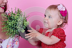 A little girl is holding a pot with a plant in her hands