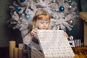 Little girl holding present near the christmas tree