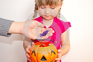 Little girl holding a pumpkin with candies in her hands, on Halloween. Grown-up people put candy to children in a pumpkin.