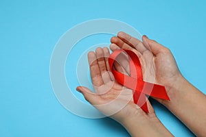 Little girl holding red ribbon on blue background, closeup with space for text. AIDS disease awareness