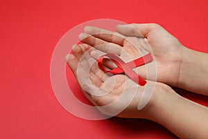 Little girl holding red ribbon on bright background, closeup. AIDS disease awareness