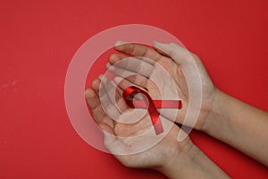 Little girl holding red ribbon on bright background, top view. AIDS disease awareness