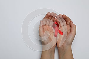 Little girl holding red ribbon on white background, top view. AIDS disease awareness