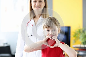 Little girl holding red toy heart in her hands in doctors office