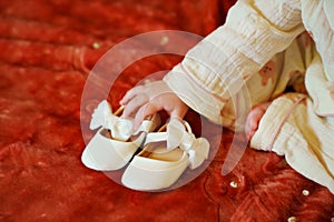 The little girl is holding small white shoes with bows in her hands.