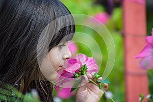 Pretty Little child Girl kid holding and smelling flower in the garden,having fun with pink flower in a beautiful clear