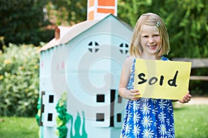 Little Girl Holding Sold Sign Outside Cardboard Playhouse