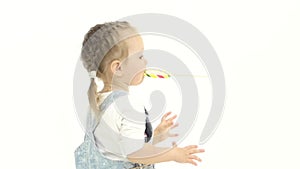 Little girl is holding a sweet candy in her hands and licks it. White background. Slow motion