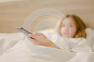 Little girl holding TV remote control in her hand while lying in bed