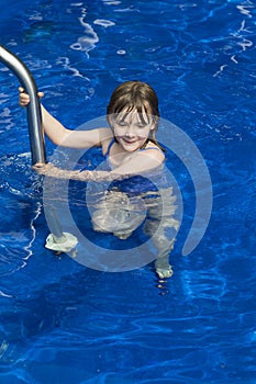 Little girl holding unto railing to step into deep blue pool photo