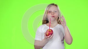 Little girl holds an apple in her hands and drinks juice from it. Green screen. Slow motion