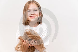 A little girl holds in hands cropped hair after cutting on a white background.