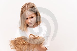 A little girl holds in hands cropped hair after cutting on a white background.