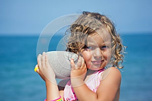 Little girl holds in hands pebble on seacoast