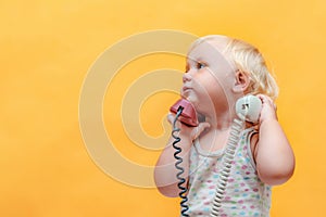 A little girl holds in her hands a tube from a wired telephone and looks around