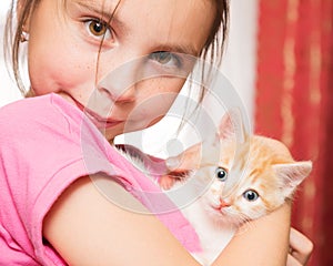 A little girl holds a kitten in her arms and hugs.