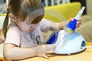 A little girl holds a nebulizer mask to inhale the medicine into her nose while at home. Treatment of colds with nasal inhalation.