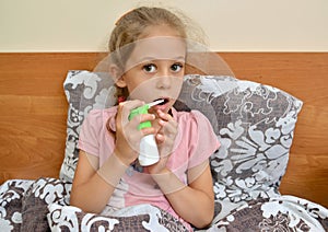 A little girl holds a spray in her hand and irrigates their throats while sitting in bed. Self-treatment photo