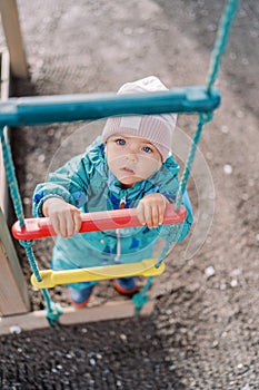 Little girl holds on to the rungs of a rope ladder and looks up. Top view