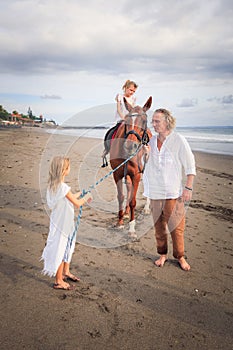 Little girl on a horse. Father and daughter leading horse by its reins on the beach. Horse riding. Family concept. Father`s day.