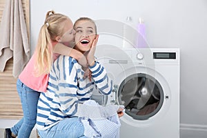 Little girl hugging her mother while she doing laundry