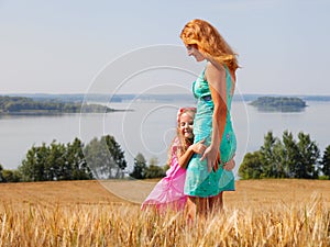 Little girl hugging her mother in a wheat field near lake