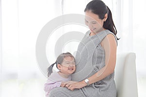 Little girl hugging her pregnant mother belly and smiles