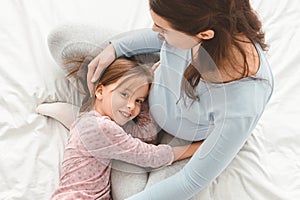 Little girl hugging pregnant mom`s belly while lying on bed