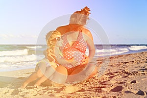 Little girl hugging pregnant mother tummy at beach