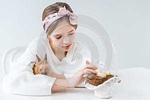 Little girl hugging rabbit and looking at basket with easter eggs in nest