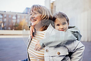 Little girl hugging smiling middle aged woman. Cute female kid and her grandmother enjoy walking outdoors