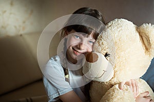 Little girl hugging teddy bear indoor in her room, devotion concept, big bear toy
