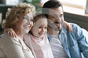 Little girl hugs father and grandmother family sitting on couch