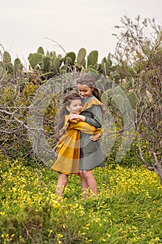 A little girl hugs her sister tightly in a thicket of branches and cactuses dressed in retro vintage old-fashioned clothes