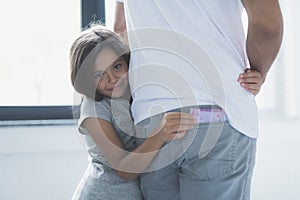 A little girl hugs a man and smiles, trying to unseen the currency from his back pocket