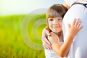 Little girl hugs mom pregnant belly