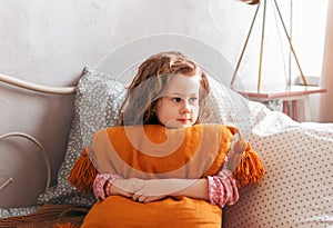 Little  girl hugs pillow on bed in children`s bedroom