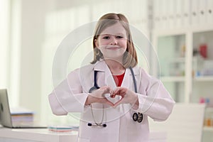 Little girl imitates role of doctor showing heart sign photo