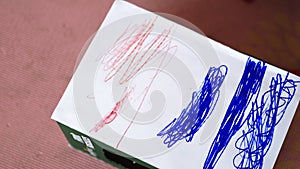 Little girl intensely coloring a white paper box with a red pencil