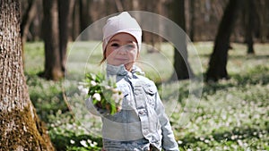 Little girl in jeans jacket standing near the tree in the forest covered with anemones