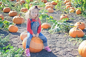 Happy girl sitting on pumpkin at farm field patch