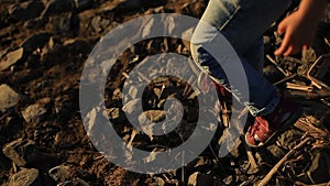 a little girl in jeans and red sandals are on large stones on the river Bank. feet close up.